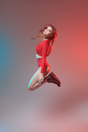 Adorable girl dancer with perfect, slim body in a red suit and black boots jumps dancing a modern...