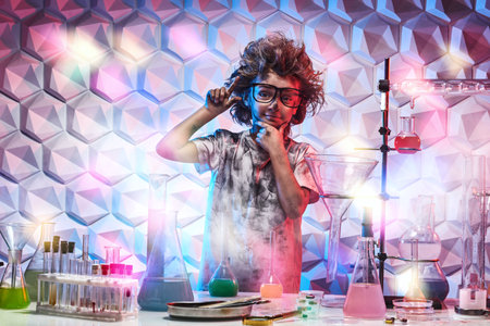 A funny little boy with glasses and matted hair stands joyfully all black after experiments in a...