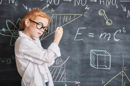 Kids and education. A smart little girl in white shirt and glasses writes formulas and diagrams on...