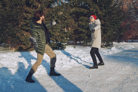 Winter activities. Two happy friends young men playing snowballs in a winter park on a sunny day. Good mood, emotions.の写真素材