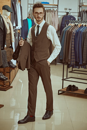 A respectable businessman in elegant classic suit and spectacles in a premium men's clothing store. Men's fashion, business style. Full length shot.の写真素材