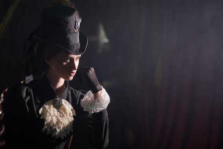 Beautiful young brunette lady in a 19th century suit stands in a dark vintage room. Historical...