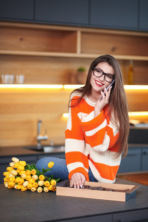 A lovely smiling girl talks joyfully on the phone while being in her cozy modern kitchen. Modern interior, furniture for the kitchen.の写真素材
