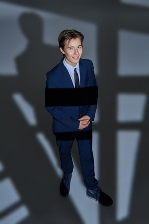 Education, student's style and fashion. Handsome confident teenage boy in classic suit smiles joyfully standing on a white background with light and shadows.の写真素材