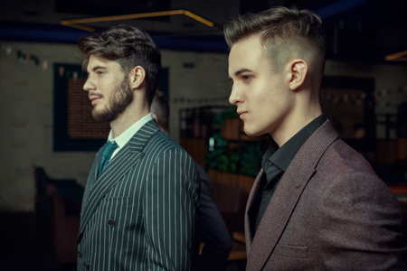 Portrait of two confident handsome young men in expensive suits standing in luxury apartments. Men's...
