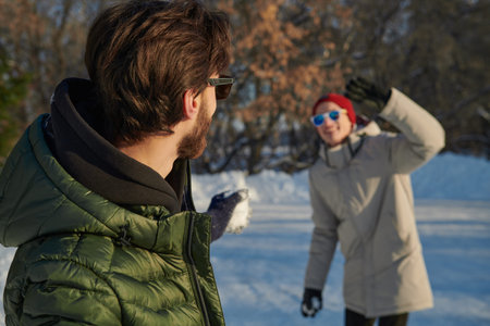 Outdoor winter activities. Two joyful friends young men playing snowballs in a winter park on a...