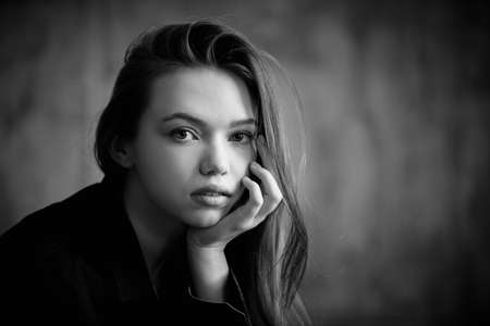 A beautiful young girl with long hair in a black shirt looking calmly at the camera. Beauty, people, emotions. Black and white shot. Psychological portrait.の写真素材