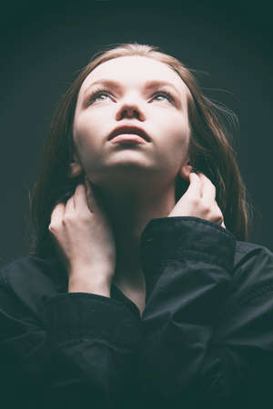 Studio shot of a beautiful young girl with long brown hair in a black shirt, looking up calmly with hope. Beauty, people, emotions.の写真素材
