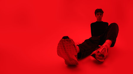 Young people and emotions. Full legth shot of a handsome moody guy sitting on the floor. Bright red...