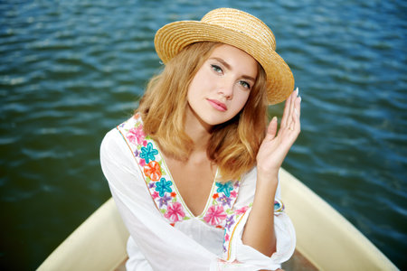 An elegant blonde girl in a white summer dress and a straw hat rides a boat on the sea. Sea resort, summer vacation. Beauty, fashion.の写真素材