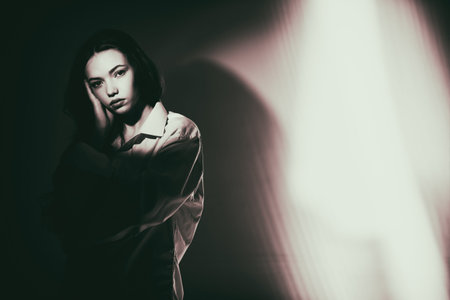 Sepia portrait of a beautiful sad girl in a white shirt, who stands thoughtfully among light and...