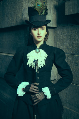 Style of the late 19th - early 20th centuries. Pretty young woman of the 19th century standing on a city street at nighttime.の写真素材