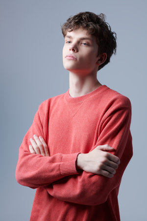 Portrait of a handsome guy model in a red sweater standing on a grey background with crossed arms....