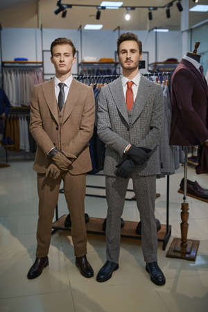 Fashionable men's clothing. Two well-groomed successful businessmen in classic suits and gloves stand in a premium men's clothing store.の写真素材