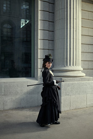 An elegant 19th century lady strolls down a city street. History and Fashion of the late 19th -...