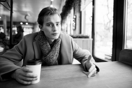 Portrait of a good-looking young man in stylish clothes warming up in a cozy cafe on a chilly winter...