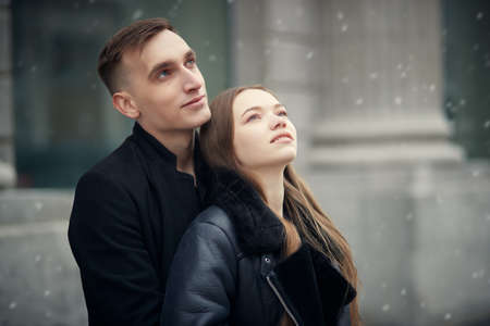 Love story. Portrait of a beautiful young people in love standing on a city street and looking joyfully at the falling snow. Young people and relationship. Winter season.の写真素材