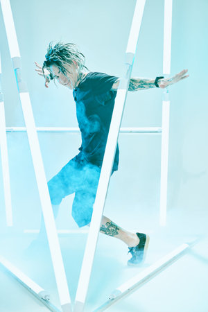 Full length portrait of an emotional punk rock musician man dancing among neon lamps surrounded by...