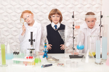 Early development of children. Three smart modern children making experiments in a chemical laboratory. Educational concept.の写真素材