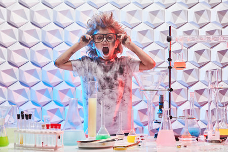 Education, science and children. A funny little boy with glasses and matted hair stands in a...