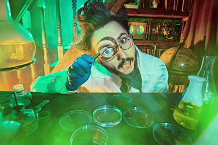 An excited crazy scientist enthusiastically conducts researches in the laboratory lit by green and...
