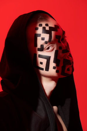 Art portrait of a young man with a QR-code painted on his face, looking unfriendly at the camera lit...