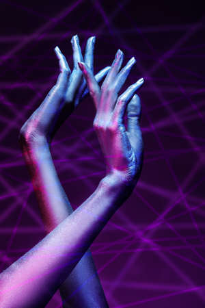 Photo of graceful thin hands with sparkling silvery skin in bright neon blue and pink lighting. Body painting, body art. Glitter makeup. Beauty industry, cosmetology.の写真素材