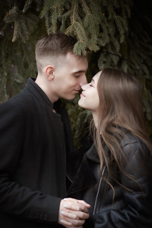 Love story. Joyful beautiful young people in love stand close to each other under a fir-tree in the...