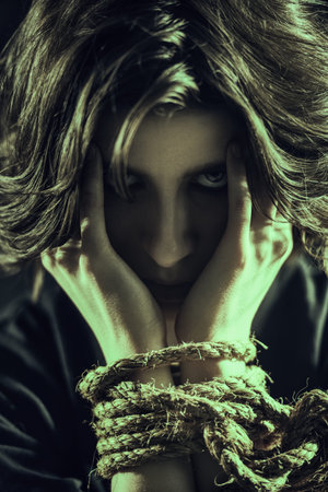 Close up shot of a brunette woman covering her face with tied hands and looking with fear at the...