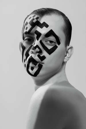 Black-and-white portrait of a young man with QR-code painted on his face who looks directly and calmly into the camera. Art concept, personification and control over a person.の写真素材