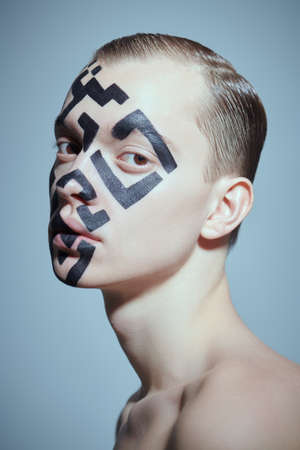 The concept of depersonalization and control over society. Portrait of a young man with a QR-code painted on his face, looking indifferently directly at the camera. Studio shot on a gray background.の写真素材