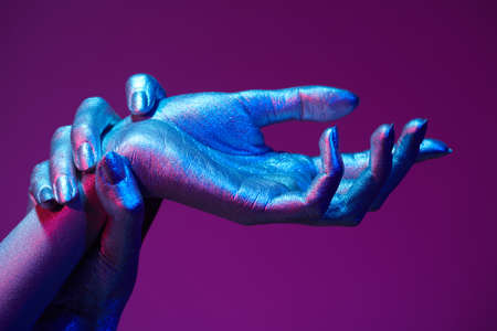 Beauty industry, cosmetology. Close-up photo of beautiful hands with sparkling silvery skin in bright neon blue and pink lighting. Body painting, body art. Glitter makeup.の写真素材