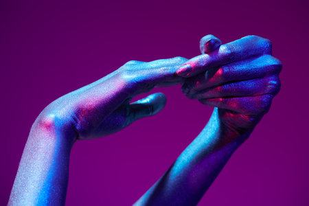 Photo of graceful thin hands with sparkling silvery skin in bright neon blue and pink lighting. Body painting, body art. Glitter makeup. Beauty industry, cosmetology.の写真素材