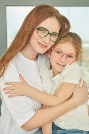 Portrait of happy, smiling mother and daughter hugging tenderly each other in the background of a window in an apartment. Happy family.の写真素材