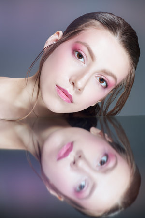 Skin care and cosmetics. A beautiful model girl with soft pink makeup poses bending down over...
