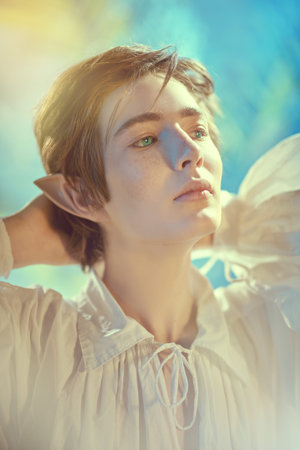 Fantasy. Handsome elf boy stands with his hands behind his head looking dreamily away. Fairy tale,...
