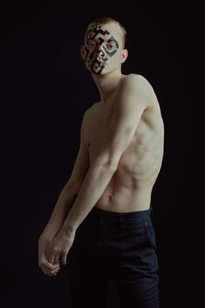 Portrait of a skinny young man with a naked torso, QR-code painted on his face and a lost look. Studio portrait on a dark background. Chipping and control over society.の写真素材