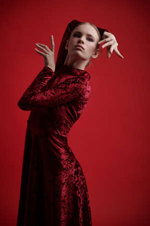 Portrait of a beautiful ballet dancer girl posing in red velvet dress on a red background in the studio. Contemporary dances, ballet.の写真素材