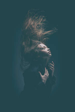 Art portrait of a beautiful young girl with long flying hair and closed eyes. The inner world of a human, emotions. Thoughtfulness, meditation. Studio portrait on a dark background.の写真素材
