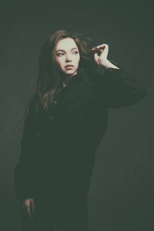 Sepia portrait of a beautiful girl with long brown hair dressed in black clothes pensively looking...