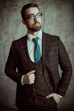 Fashion shot. Portrait of an elegant handsome man in fashionable three-piece suit and a tie posing in the background of a gray grunge wall.の写真素材