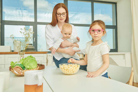 Portrait of mother in a cozy kitchen at home with her two children. Kitchen design, furniture for kitchen. Happy modern family.の写真素材