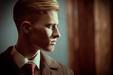 Close up shot of a handsome blond man in a coat and formal suit standing in a vintage room and...