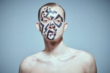 The concept of depersonalization and control over society. Portrait of a young man with a QR-code painted on his face, looking indifferently at the camera. Studio shot on a gray background.の写真素材