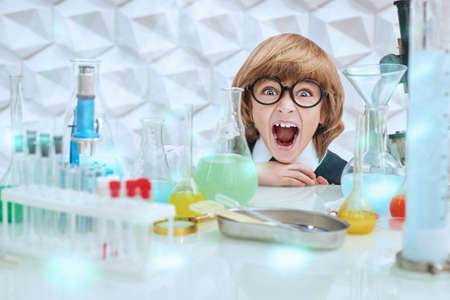 School and education. A smart boy in neat school uniform and glasses making science experiments in the laboratory and screaming.の写真素材