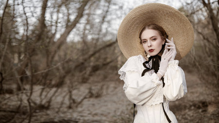 Victorian style. Portrait of a beautiful romantic girl in a white dress and a straw hat in an old autumn park.の写真素材