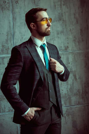 Fashion shot. Portrait of an elegant handsome man in fashionable three-piece suit and a tie posing in the background of a gray grunge wall.の写真素材