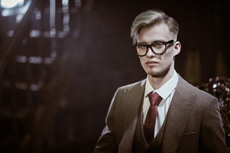 A handsome young man in an expensive three-piece suit sitting in an armchair in luxury apartments with classic interior. Men's beauty, fashion. Copy space.の写真素材