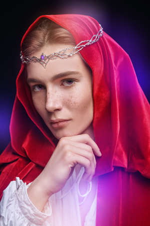 Portrait of a young handsome prince of elves wearing a red velvet cloak and a crown. Studio portrait on a black background. Fairy tale, magic. Fantasy.の写真素材