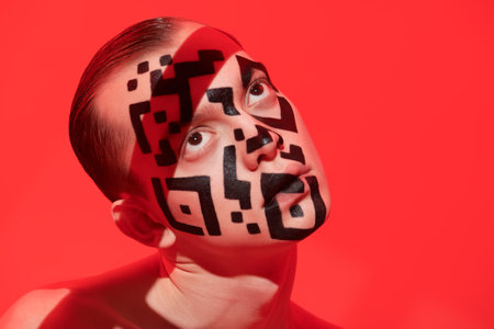 Close up shot of a young man with a QR-code painted on his face looking indifferently up on a red...